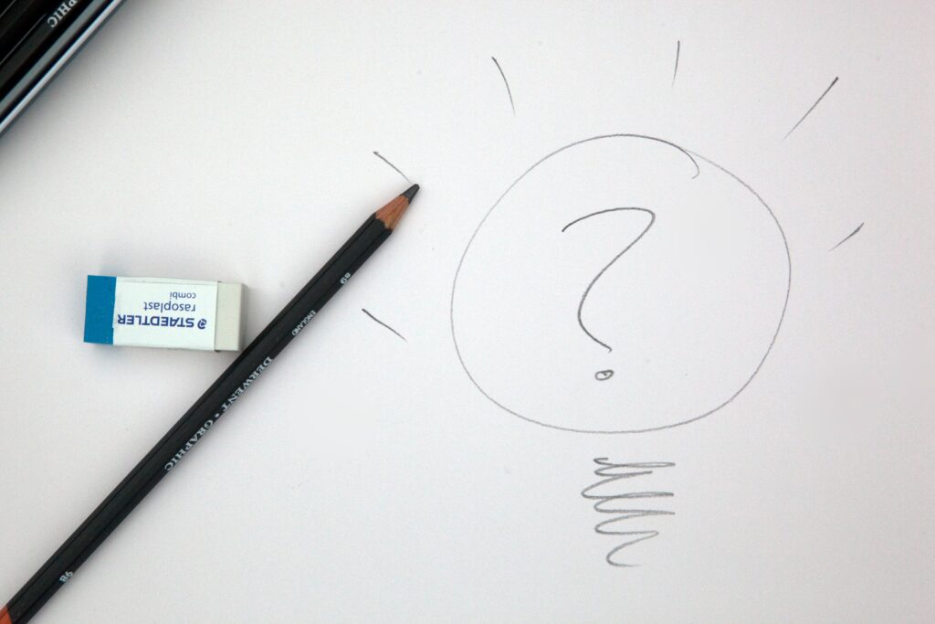 A pencil and a marker on paper with a question mark drawn in it.