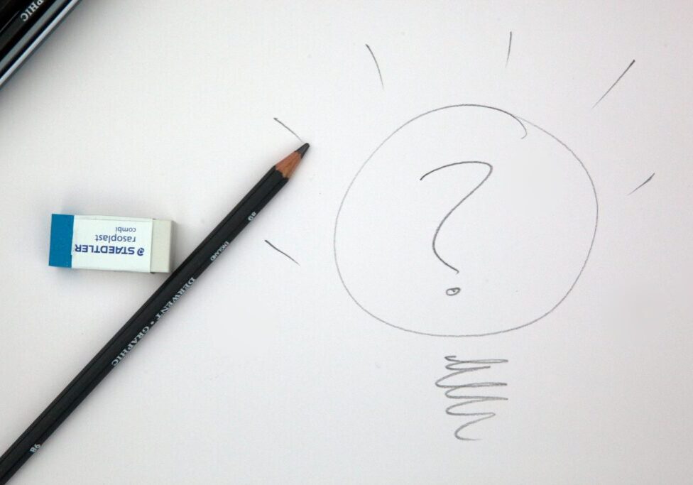 A pencil and a marker on paper with a question mark drawn in it.